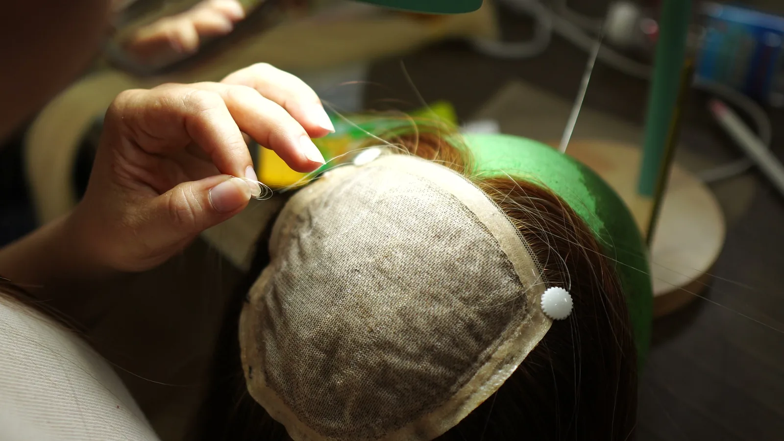 Detail of a partially hand-tied wig cap on a wig block