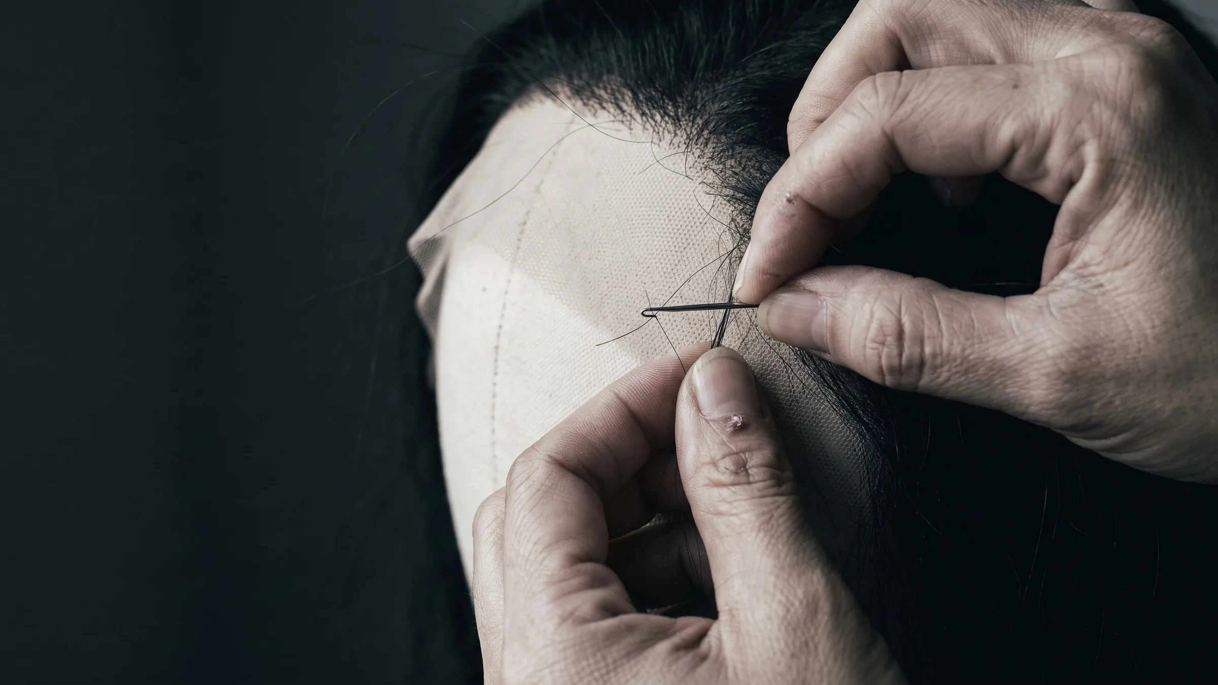 Artisan hand-tying human hair into a lace wig cap