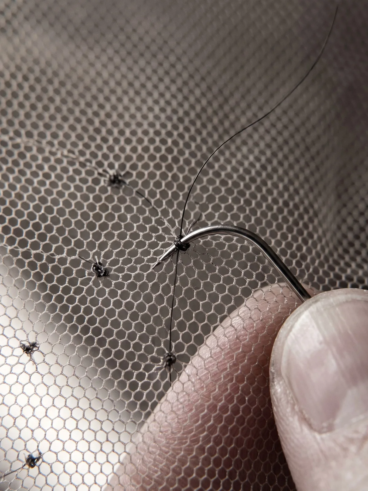 Ventilating needle drawing a hair strand through lace mesh